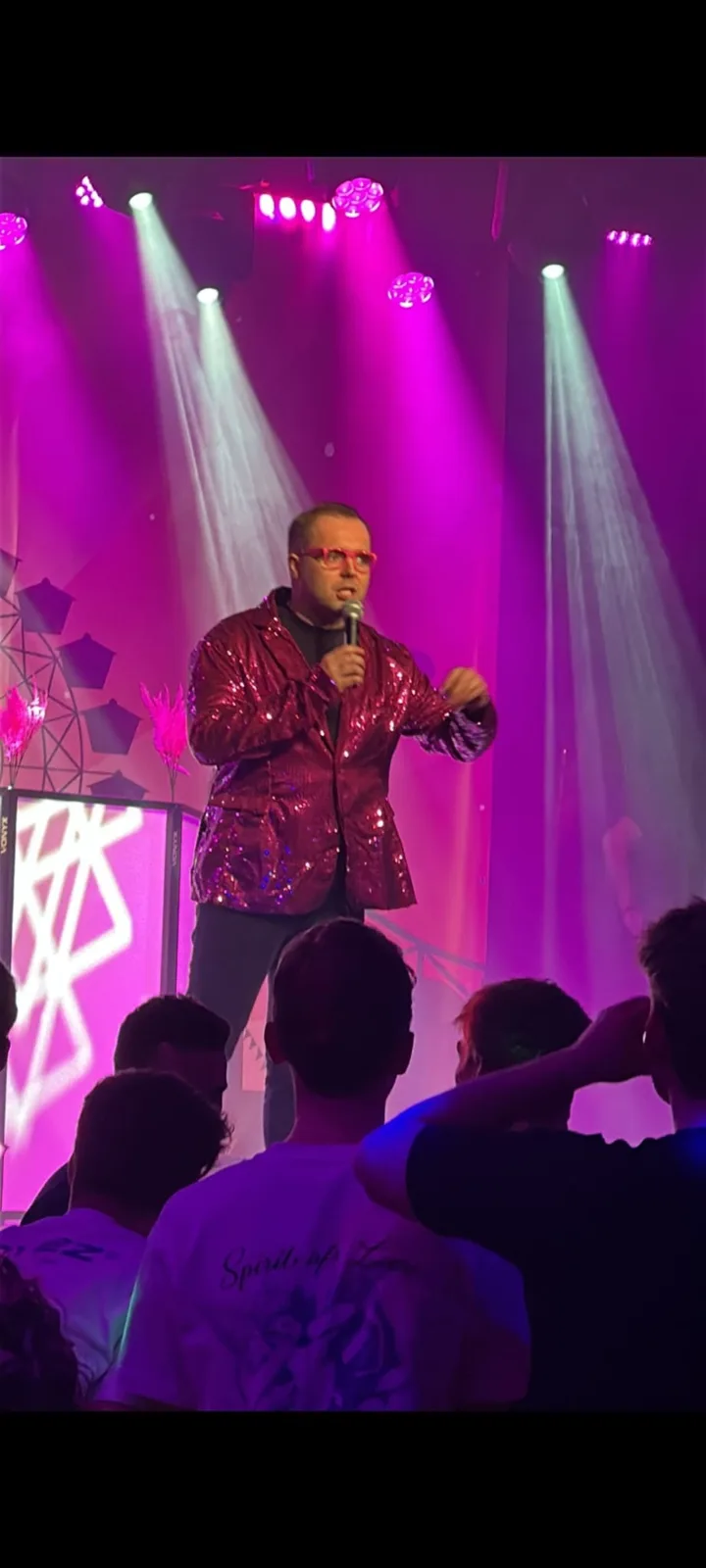 Zanger Mark Schokker zingt in een rood glitterjasje op een podium onder roze licht