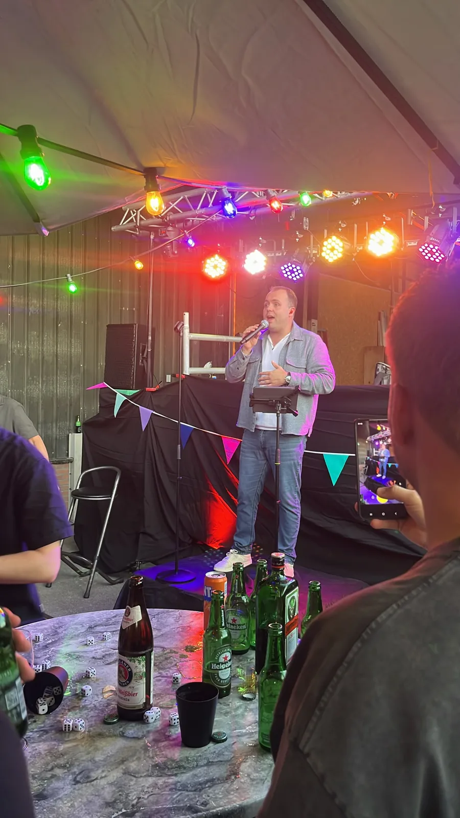 Zanger Mark Schokker zingt op een podium in een feesttent met gekleurde lampen en vlaggetjes