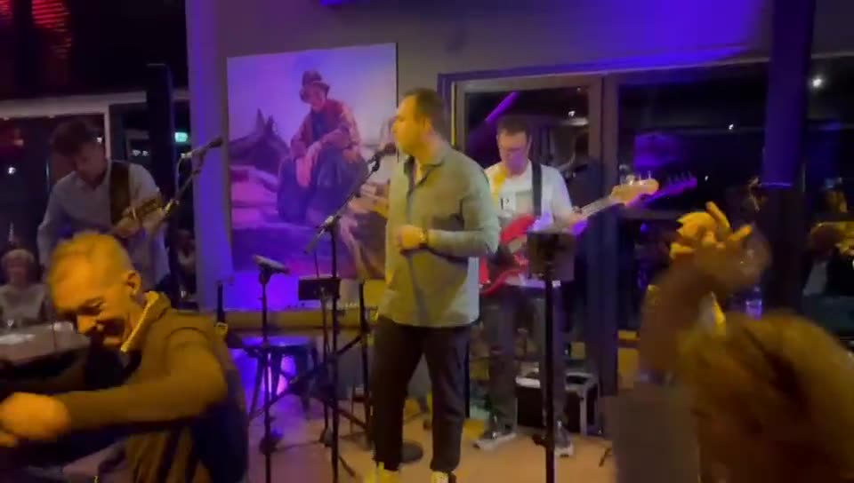 Zanger Mark Schokker in een klein café met live gitaristen en paars licht