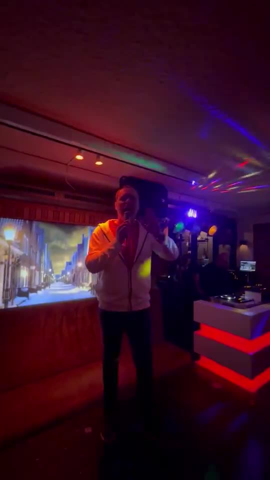 Zanger Mark Schokker zingt onder rood licht op de vloer bij het publiek in een kroeg met ledschermen