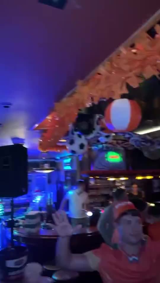 Zanger Mark Schokker in een volle kroeg in het oranje, met handen in de lucht