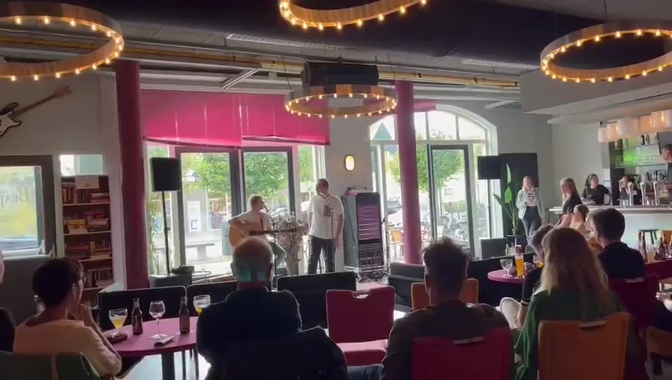 Zanger Mark Schokker zingt in een feestzaal met volle tafels, gefilmd van verder weg
