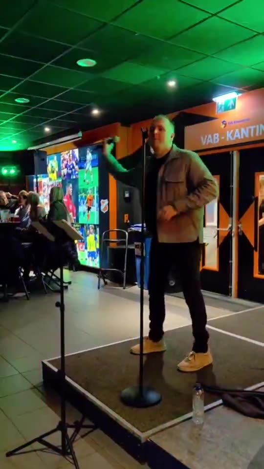Zanger Mark Schokker zingt solo op een klein podium met wisselend licht in de kantine van een vereniging